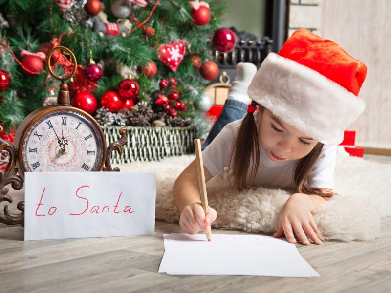 Pretty girl in Santa hat writes letter to Santa